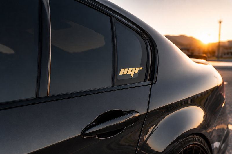 Load image into Gallery viewer, A close-up of a glossy black car at sunset, showing the rear side window with a gold 'mqr' decal applied to the glass.
