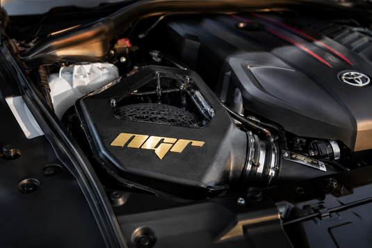 A close-up of a car engine bay featuring a black intake component with a gold N2F logo, set against a dark engine cover with a visible Toyota emblem.